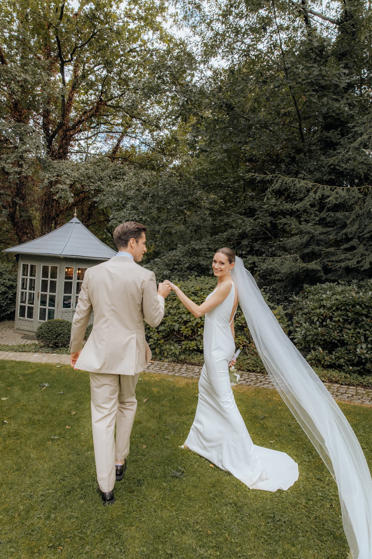 Brautpaar spaziert Hand in Hand durch den Garten der Hochzeitslocation