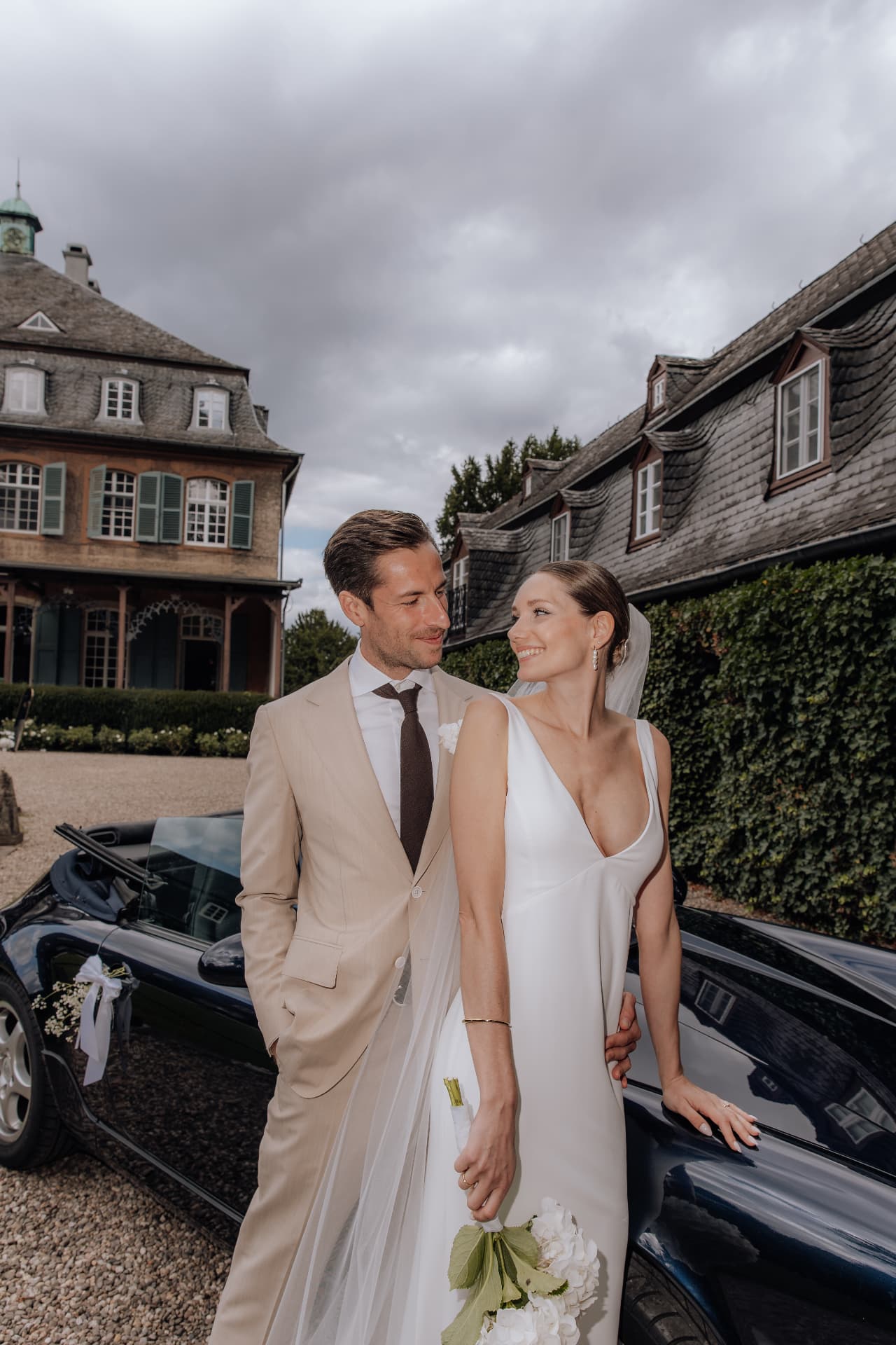 Brautpaar am Hochzeitsauto vor dem historischen Anwesen